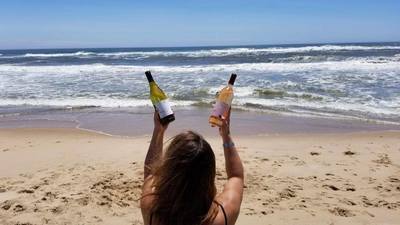 A woman holding two bottles of wine on the beach during her Hamptons weekend vacation. 